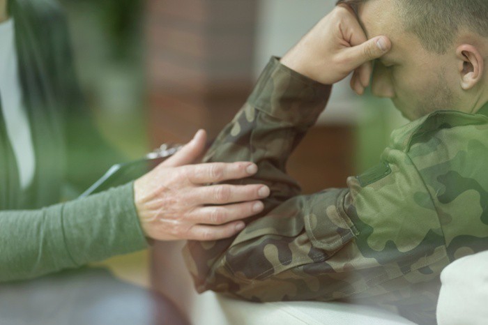 A uniformed soldier with his head lowered is sitting with a therapist