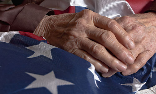 An elderly man places his hands on an American flag